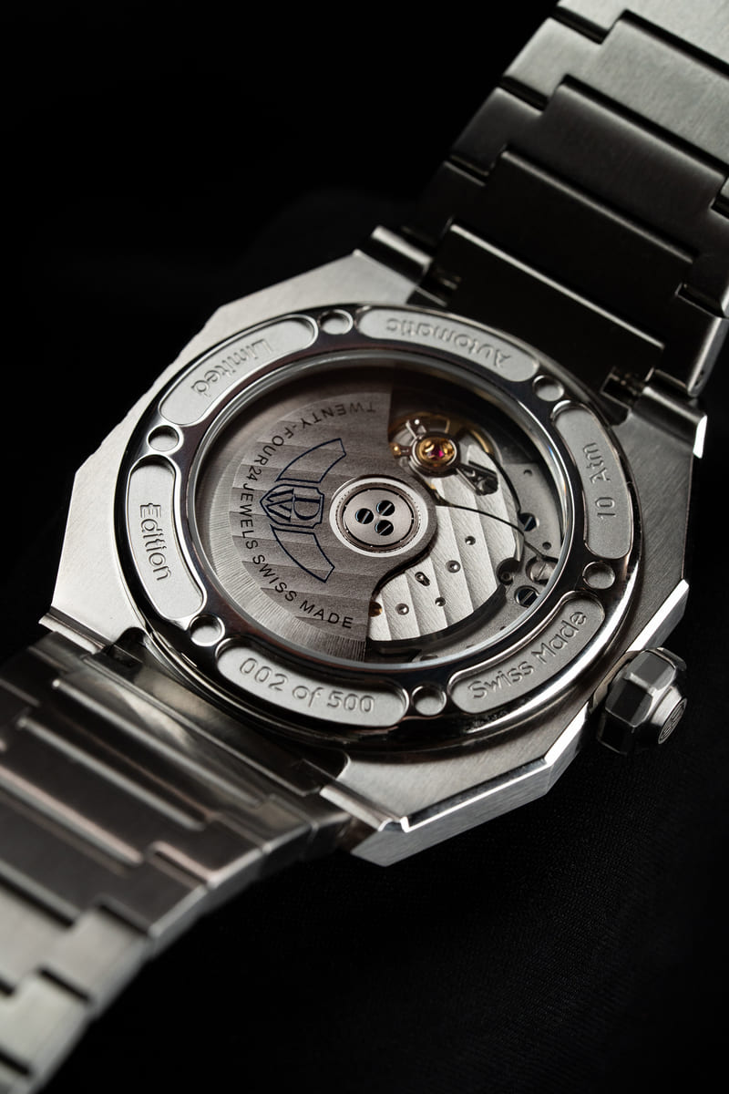 Close-up of the DWISS A1 automatic watch from the back, featuring a transparent sapphire caseback, visible rotor, engraved markings, and a stainless steel bracelet on a dark background.